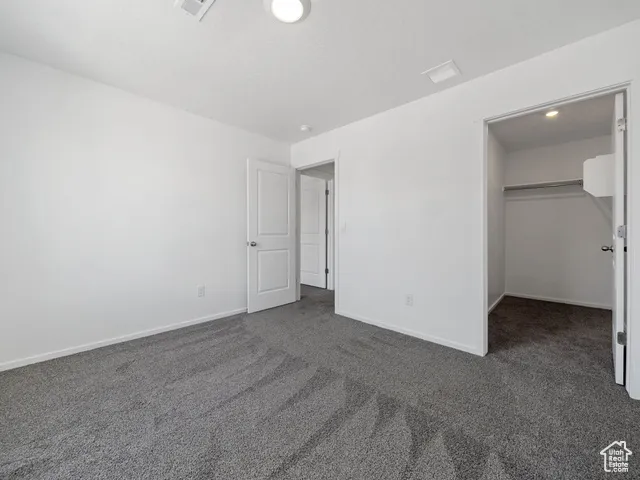 Unfurnished bedroom featuring a walk in closet and dark colored carpet