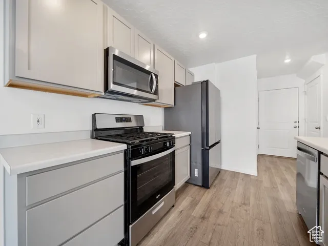 Kitchen with appliances with stainless steel finishes, light countertops, light wood finished floors, recessed lighting, and gray cabinetry
