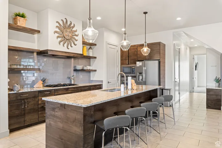 Kitchen with open shelves, tasteful backsplash, light stone countertops, hanging light fixtures, and recessed lighting
