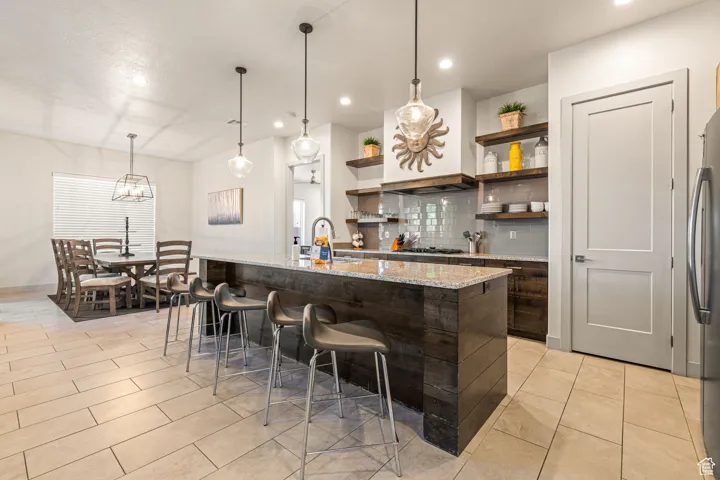 Bar area with hanging light fixtures, open shelves, light stone countertops, dark brown cabinetry, and recessed lighting