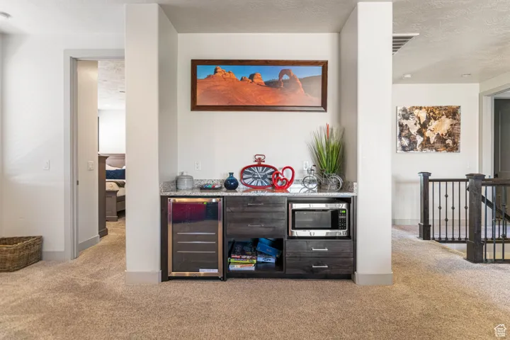 Indoor dry bar with light carpet, beverage cooler, a textured ceiling, and stainless steel microwave