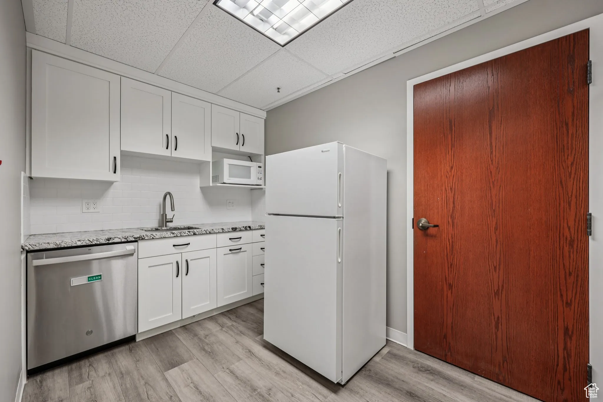 Kitchen with white appliances, a paneled ceiling, decorative backsplash, white cabinetry, and light wood-type flooring