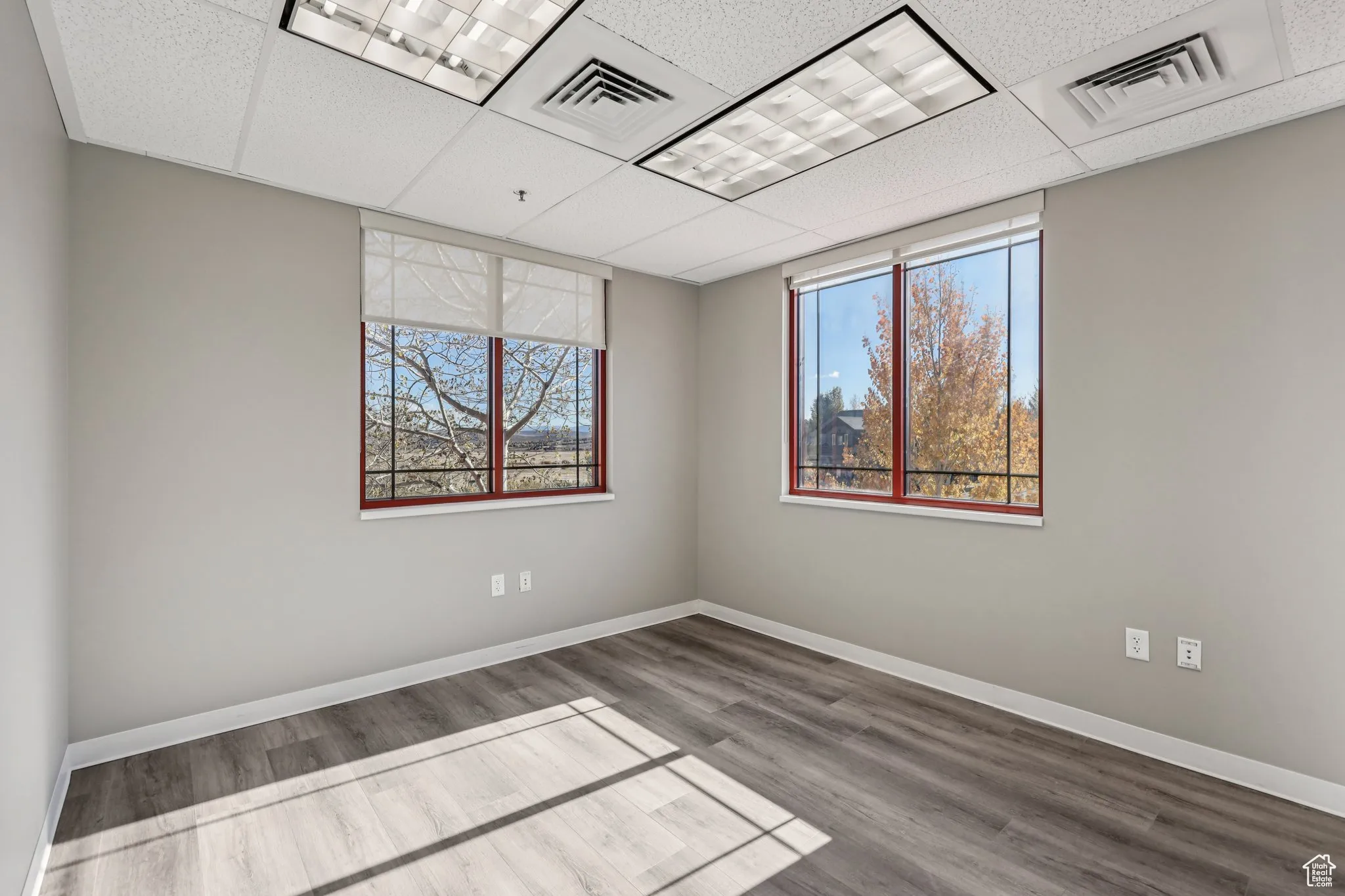 Empty room with a drop ceiling, wood finished floors, and plenty of natural light