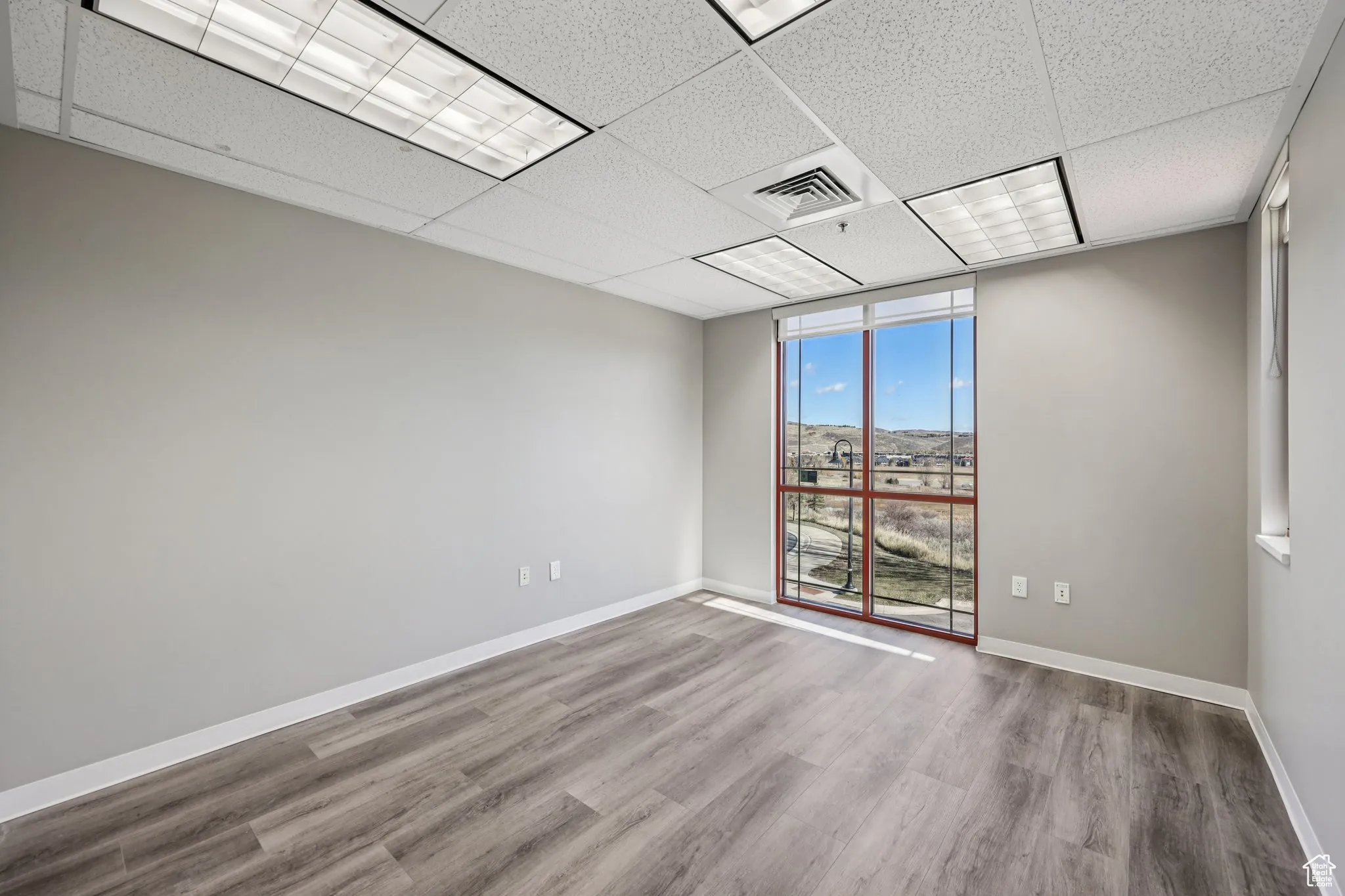 Spare room with a paneled ceiling, wood finished floors, and a wall of windows