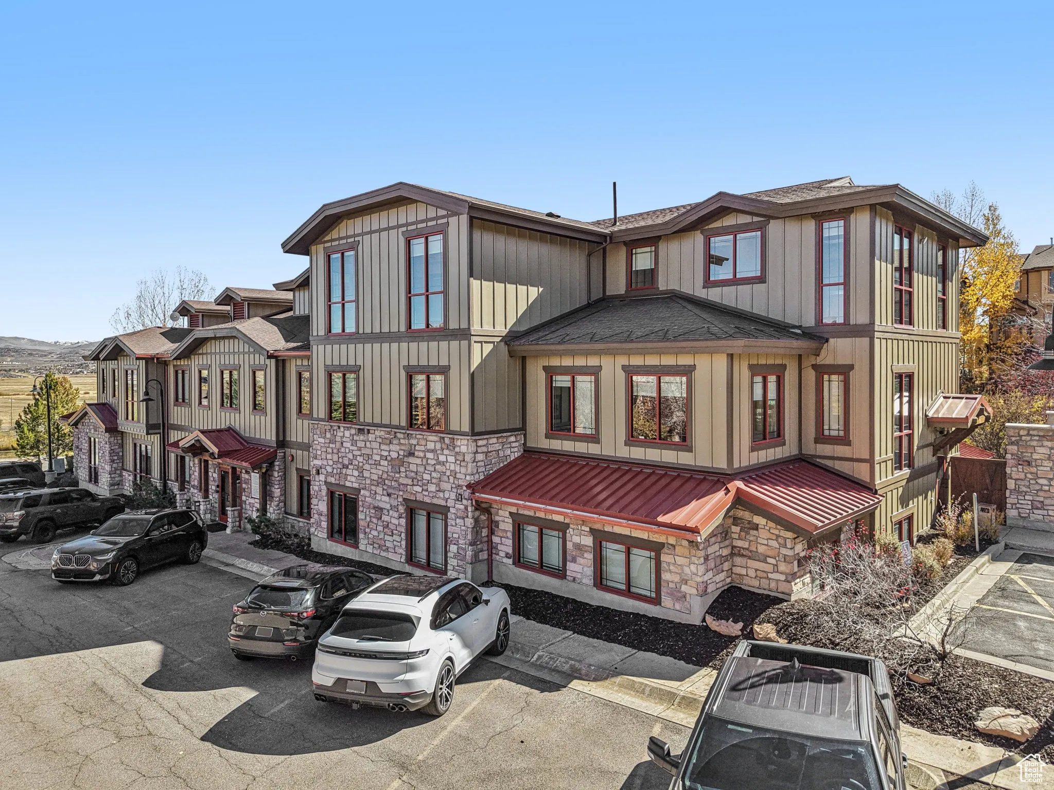 View of front facade with a standing seam roof, a metal roof, uncovered parking, board and batten siding, and stone siding
