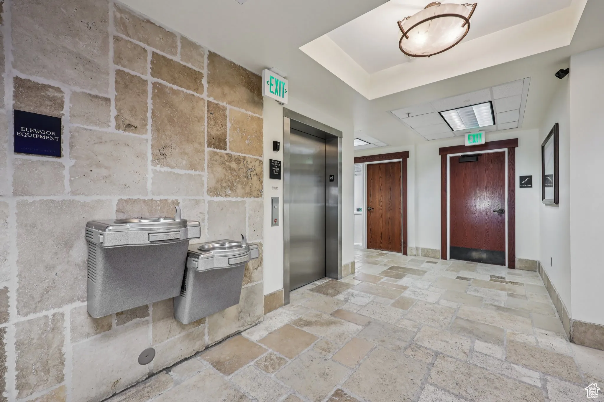 Corridor featuring stone tile floors, elevator, and a raised ceiling