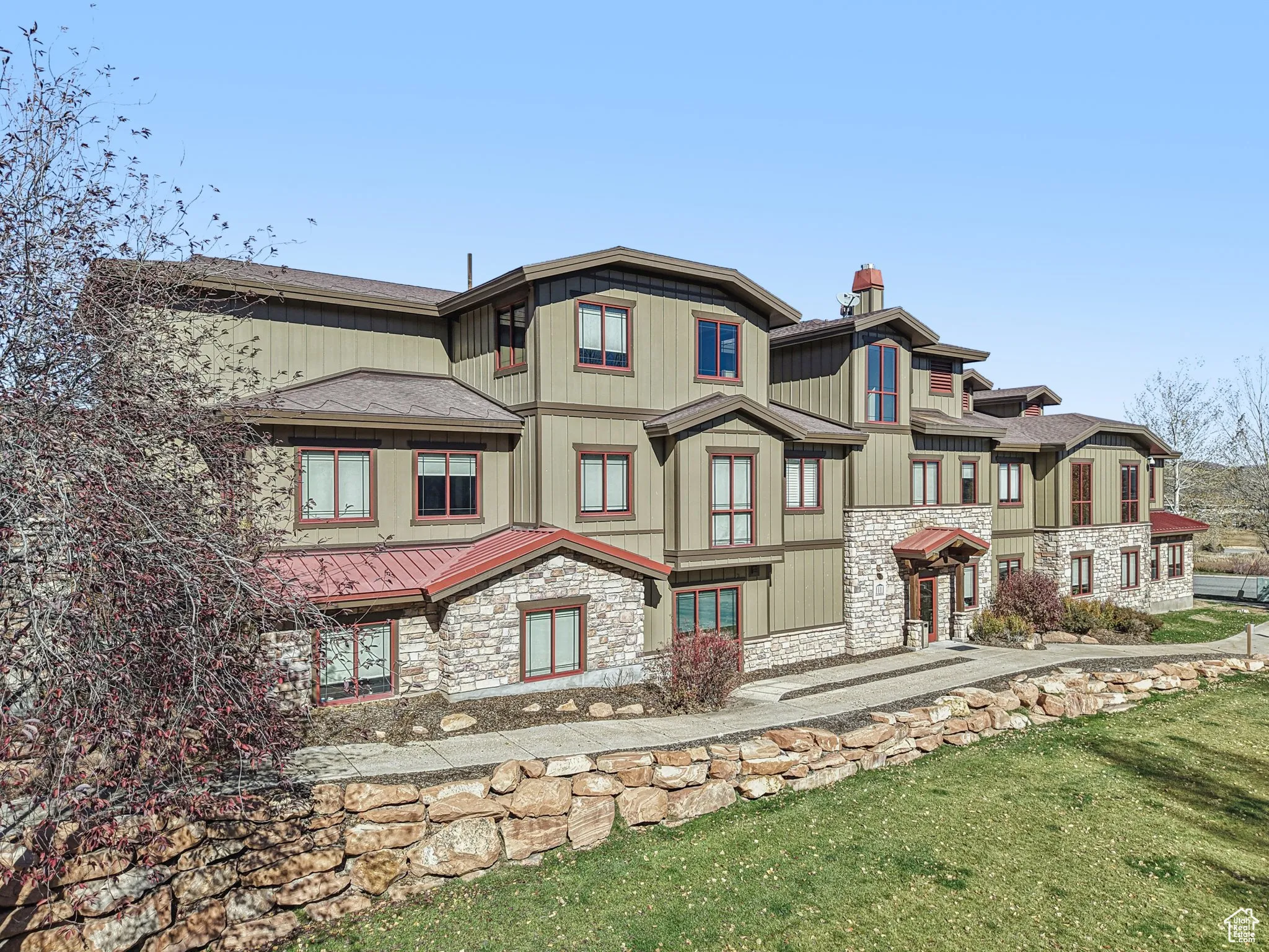 View of front facade with stone siding, a chimney, a front yard, a metal roof, and roof with shingles