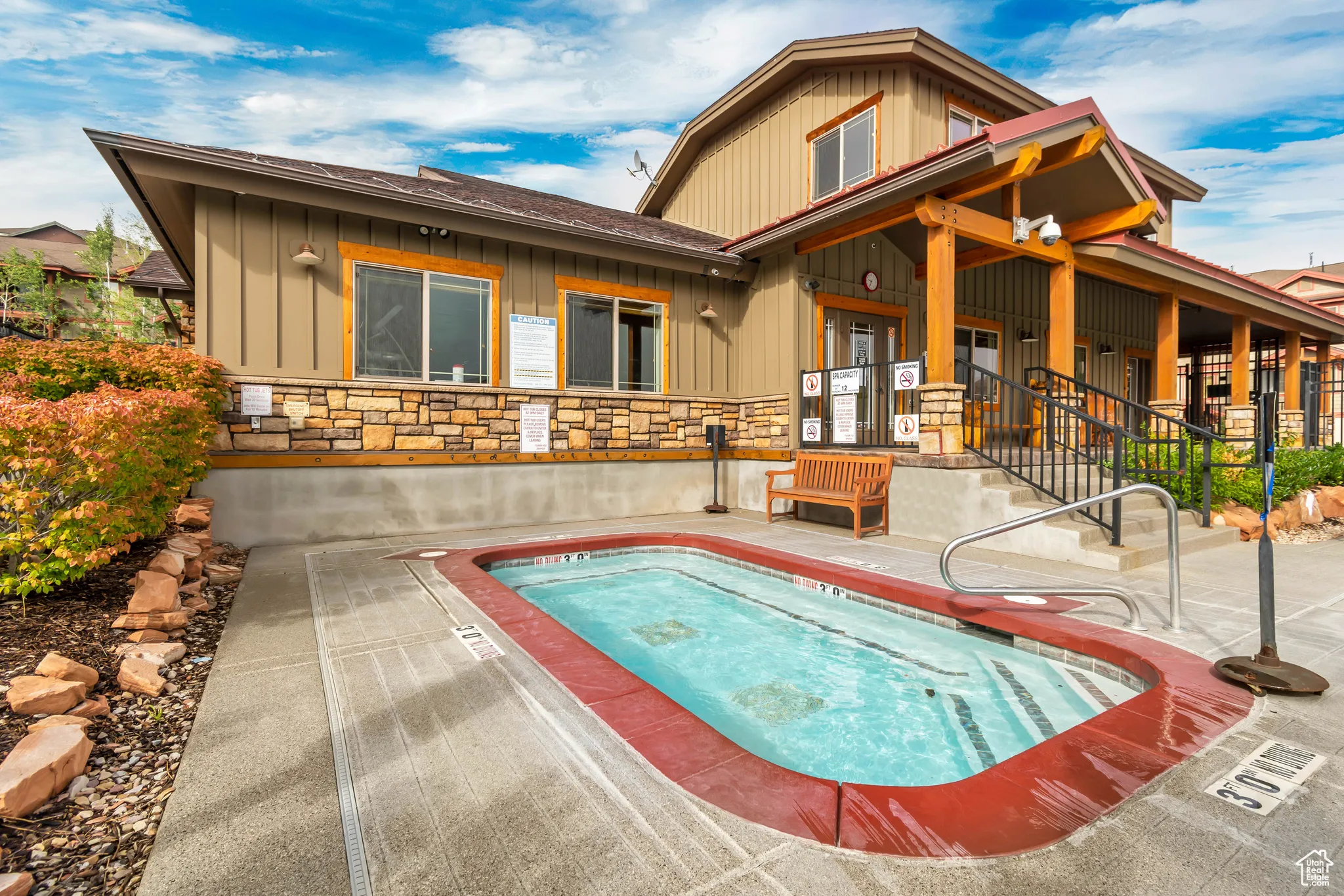 Back of house featuring stone siding, board and batten siding, a hot tub, and a patio