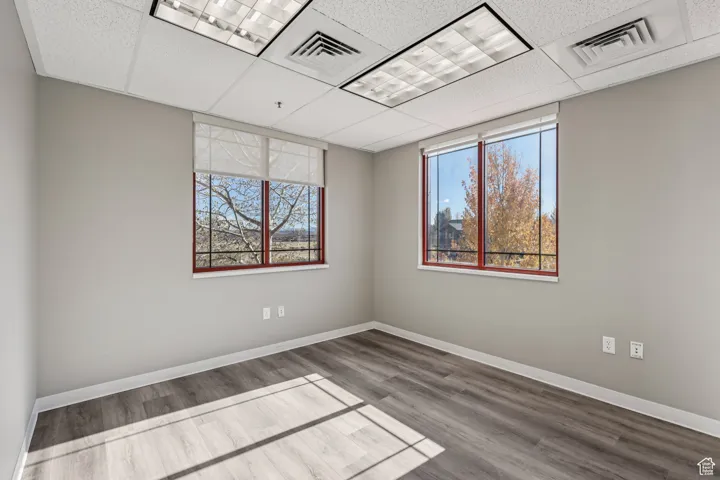 Empty room with a drop ceiling, wood finished floors, and plenty of natural light