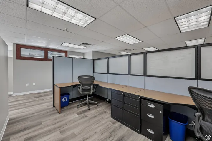 Office space with light wood finished floors, a paneled ceiling, and built in study area