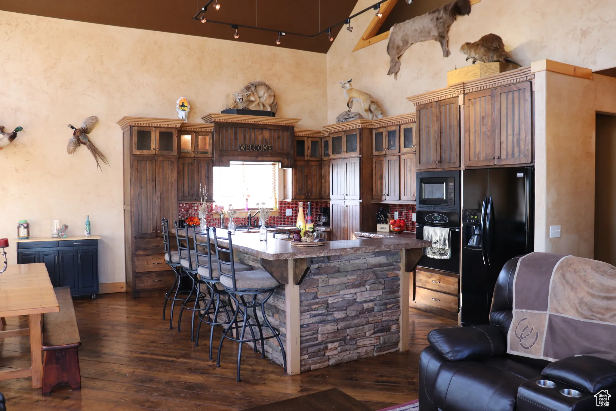 Kitchen featuring a kitchen breakfast bar, black appliances, a center island with sink, glass insert cabinets, and a towering ceiling