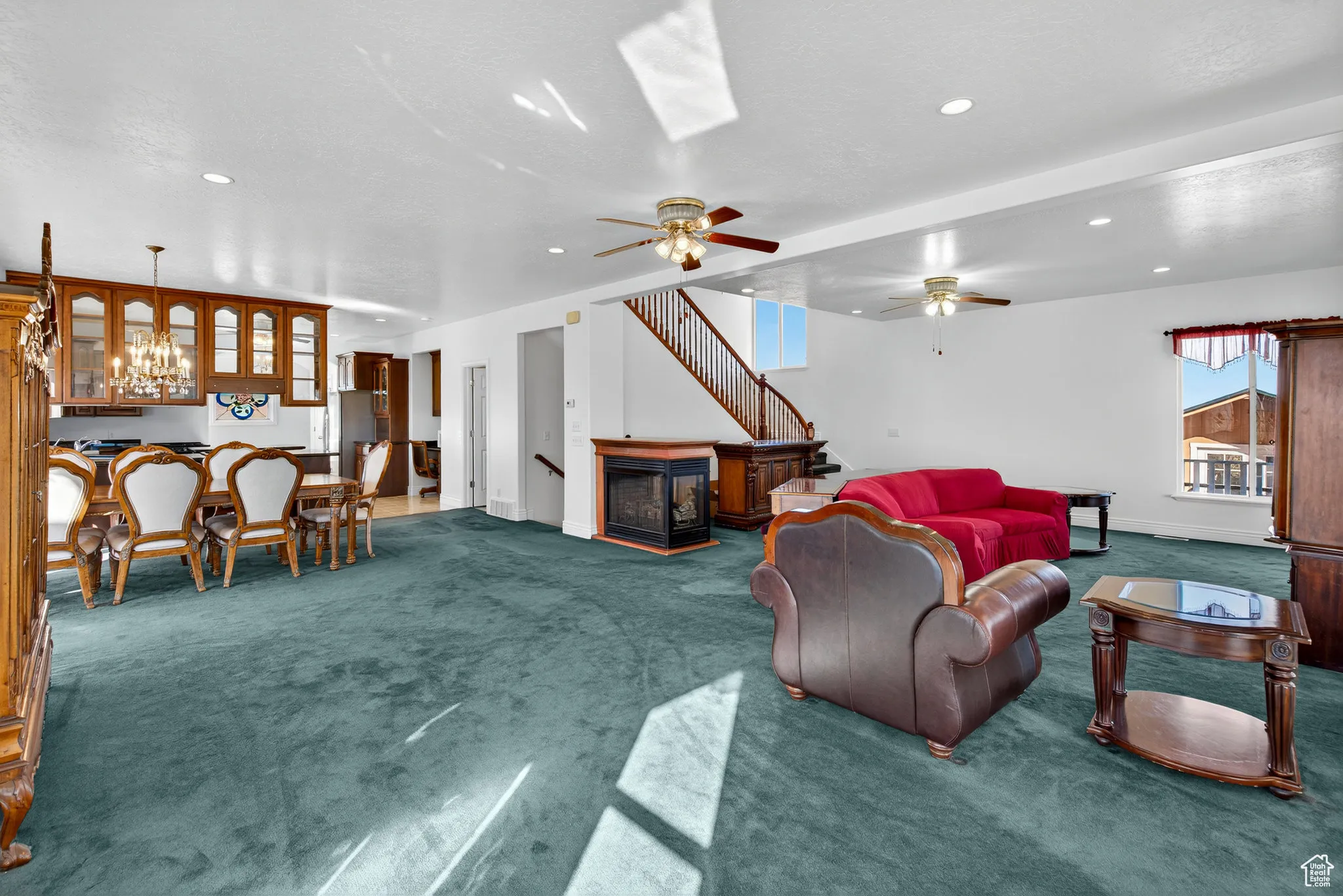Living room with carpet, ceiling fan, a chandelier, recessed lighting, and stairs.