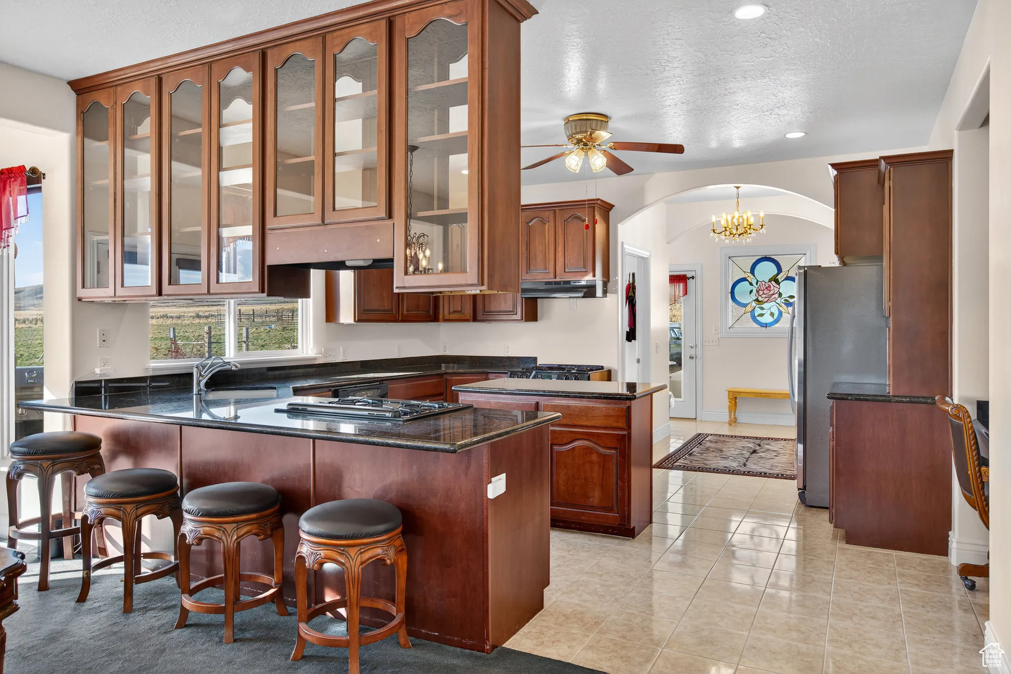 Kitchen with a peninsula, arched walkways, dark stone counters, stainless steel fridge, and light tile patterned floors.