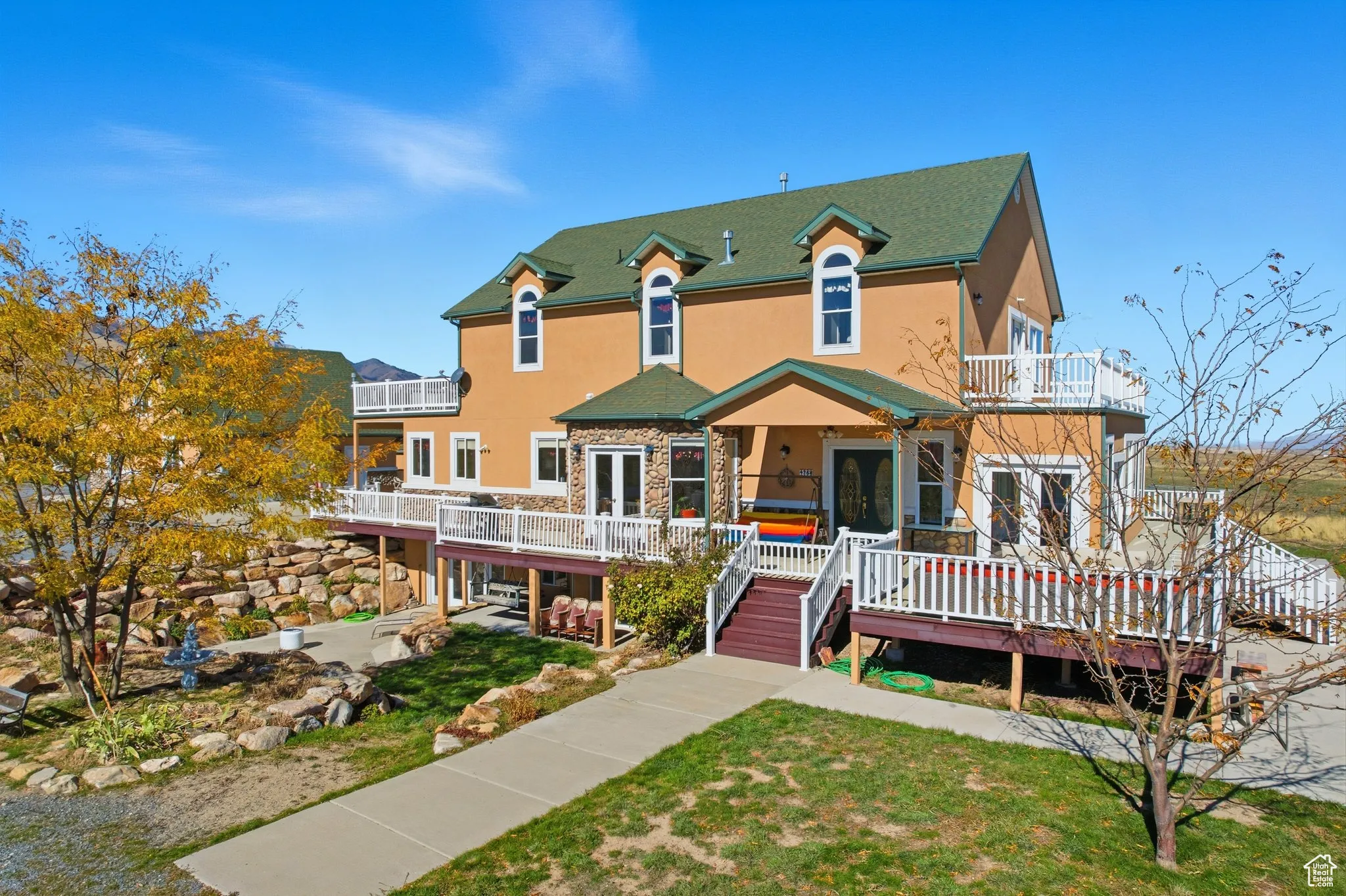 View of south side of home with stucco siding, a deck, a lawn, stairs, and a balcony.