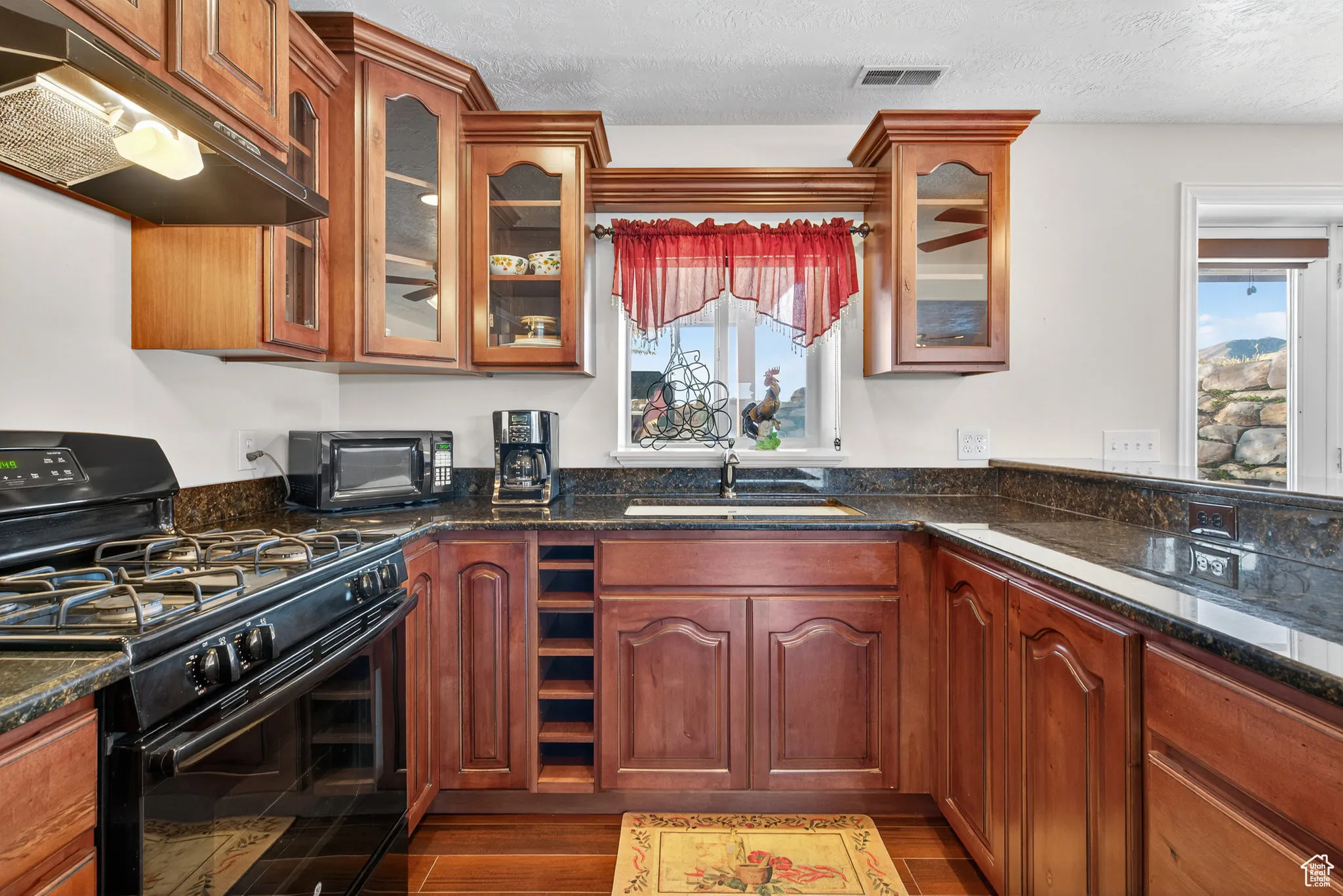 Basement kitchen with gas stove, dark stone countertops, under cabinet range hood, dark wood-style floors.