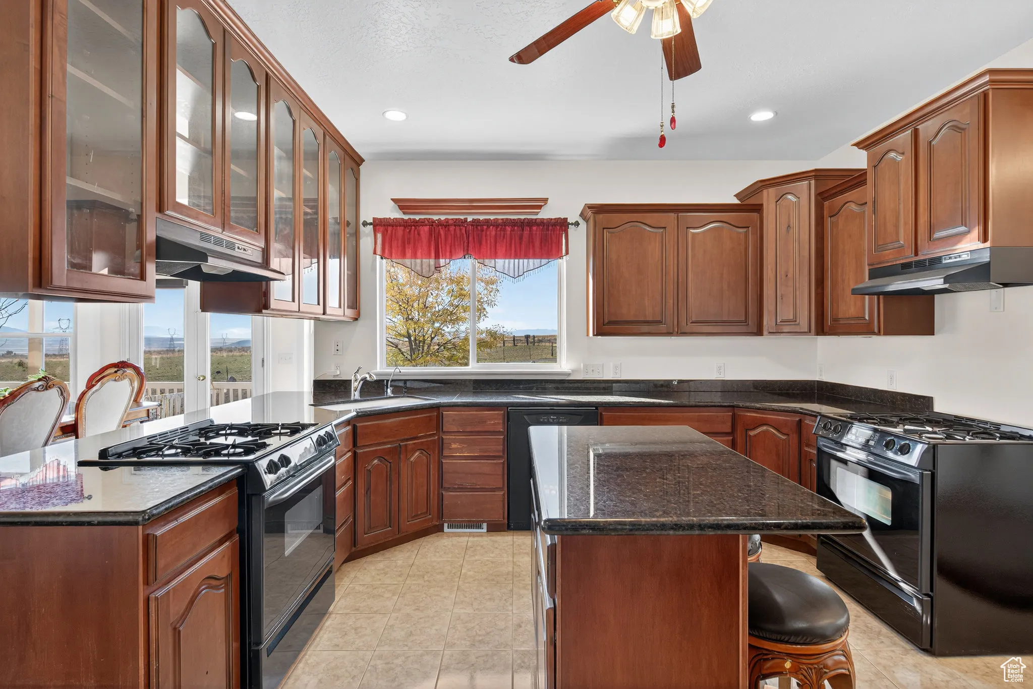 Kitchen featuring black appliances, dark stone counters, glass insert cabinets, and under cabinet range hoods.