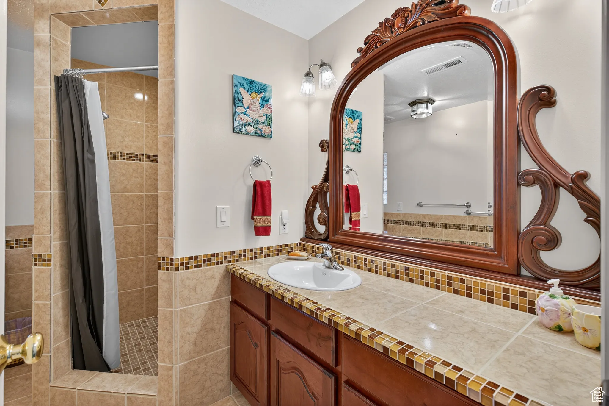 Basement bathroom with a tile shower, vanity, tile walls, and light tile patterned flooring.