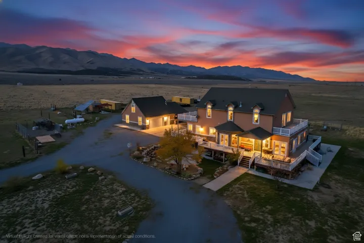 South side of house at dusk featuring driveway, a balcony, a deck with mountain view, and a yard.