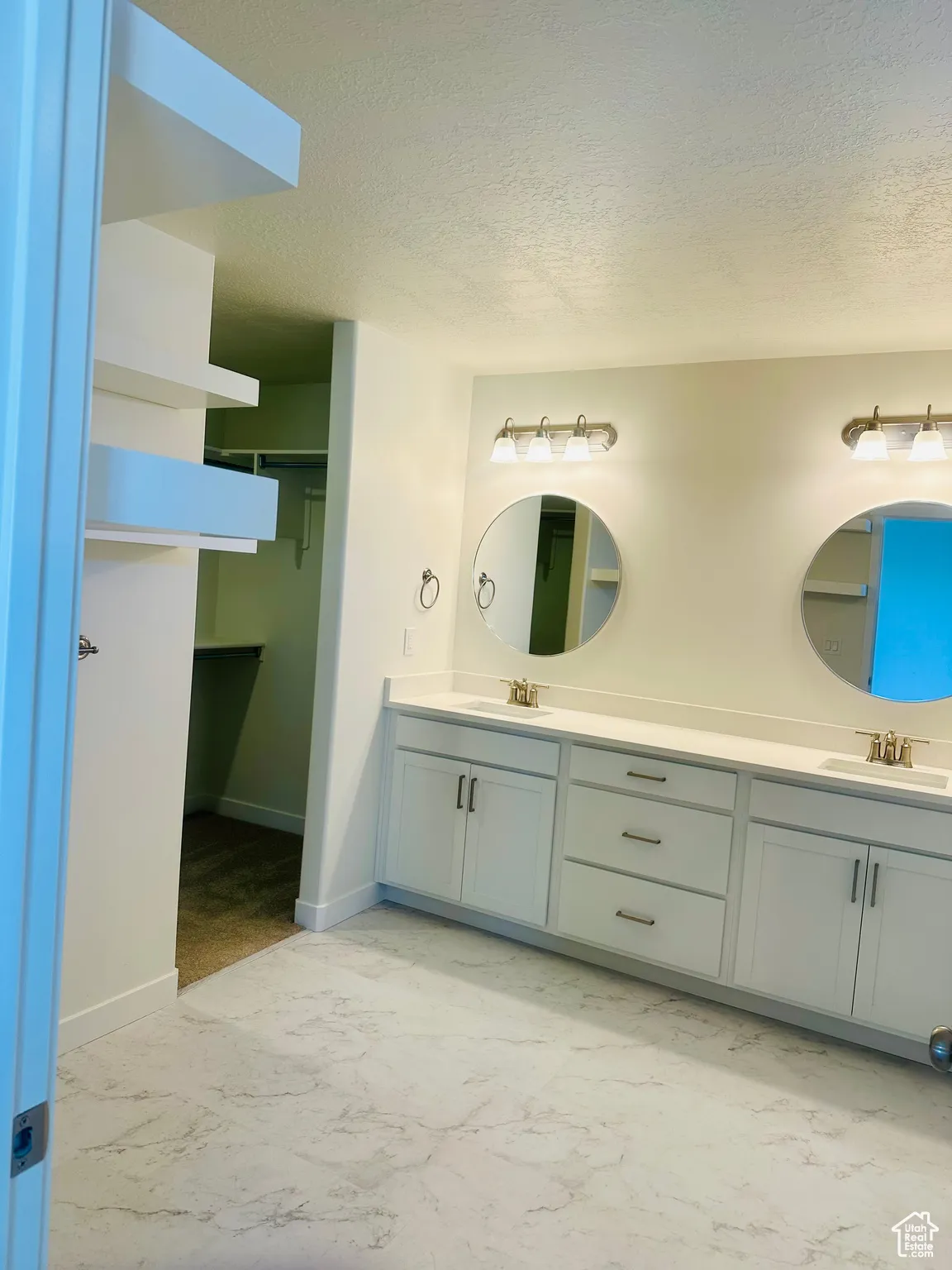 Bathroom featuring a textured ceiling, a walk in closet, double vanity, and light marble finish flooring