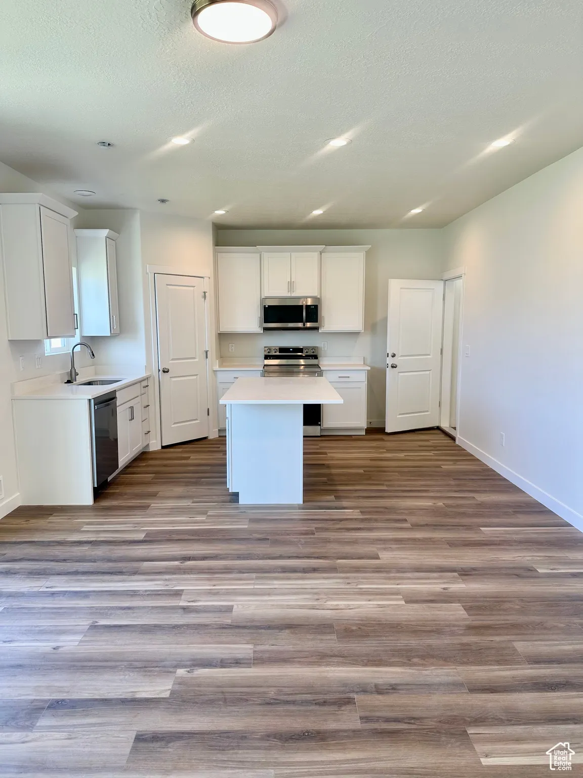 Kitchen with white cabinets, light countertops, stainless steel appliances, dark wood-style floors, and a textured ceiling