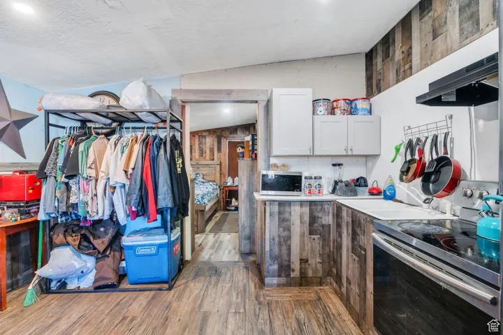 Kitchen featuring stainless steel appliances, dark wood-type flooring, white cabinetry, ventilation hood, and lofted ceiling