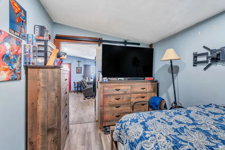Bedroom with vaulted ceiling, light wood-type flooring, and a barn door