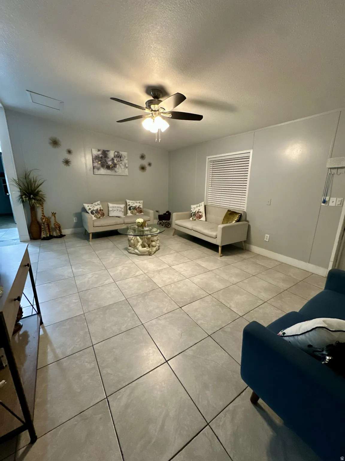 Living area featuring a textured ceiling, light tile patterned flooring, and a ceiling fan