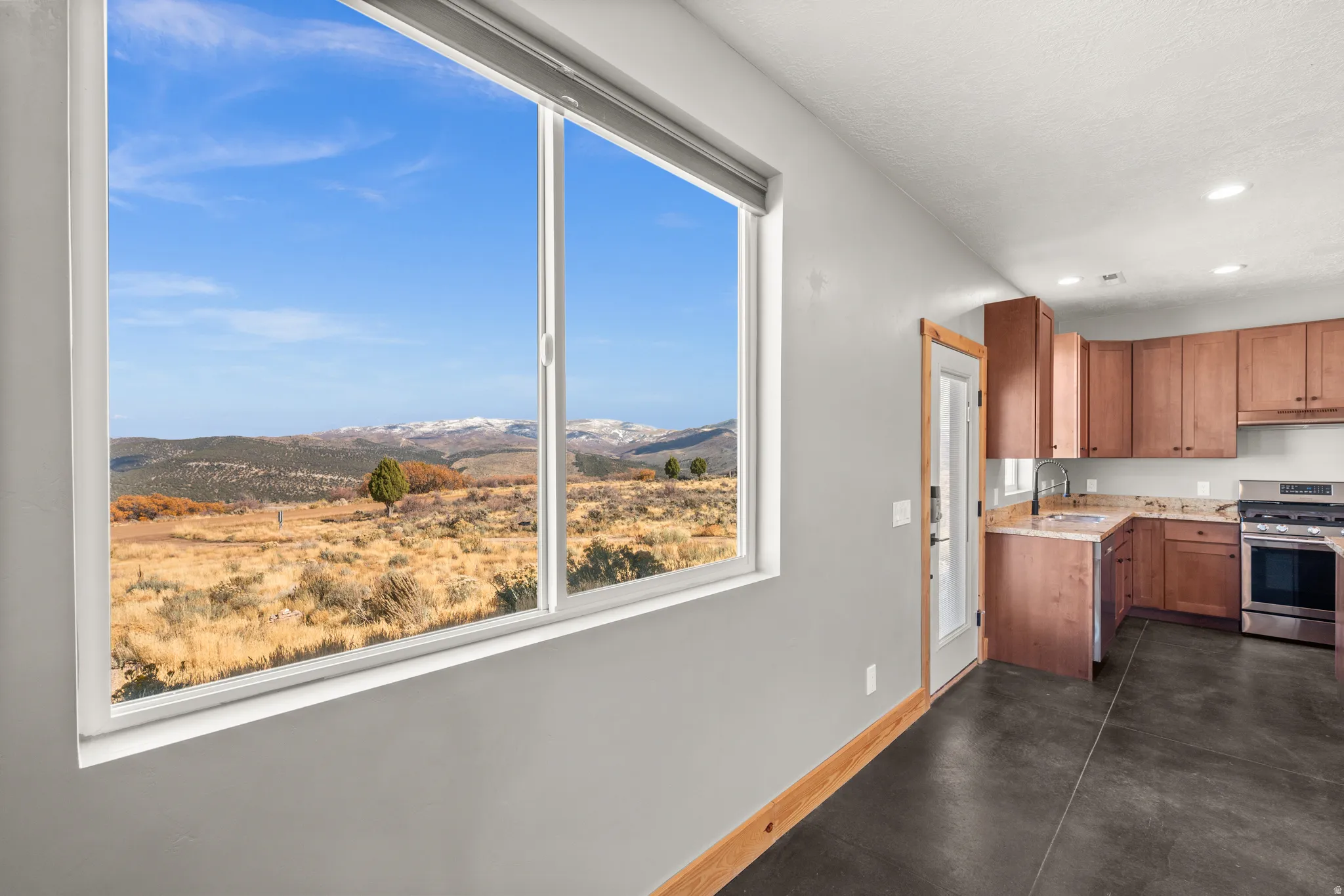 Kitchen with stainless steel range with gas stovetop, a mountain view, brown cabinets, recessed lighting, and concrete flooring