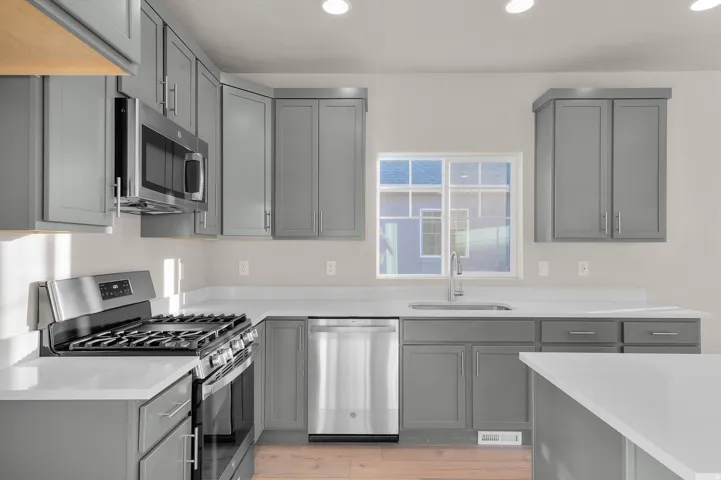 Kitchen featuring gray cabinetry, appliances with stainless steel finishes, recessed lighting, light wood-type flooring, and light stone counters