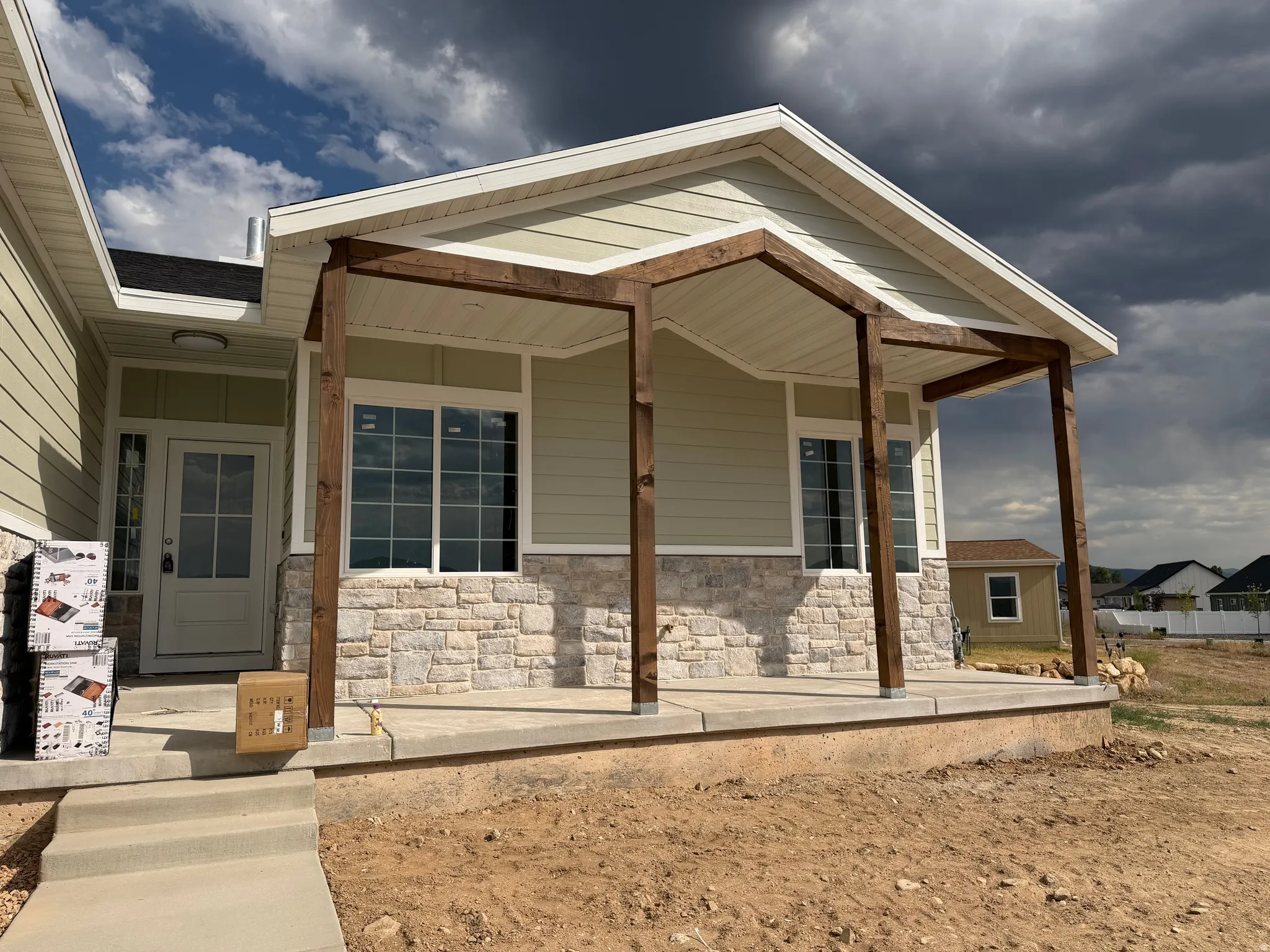 Front exterior featuring light green siding, a stone veneer foundation, a covered porch with dark wood posts, and a white paneled entry door