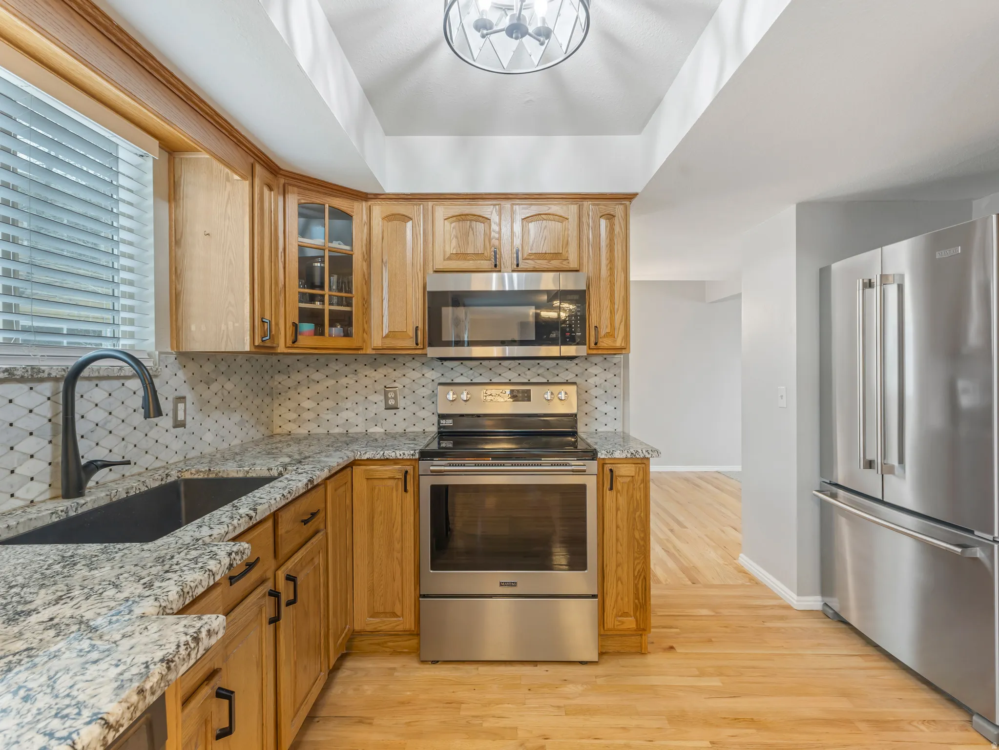 Kitchen featuring stainless steel appliances, light stone countertops, glass insert cabinets, and light wood-style flooring