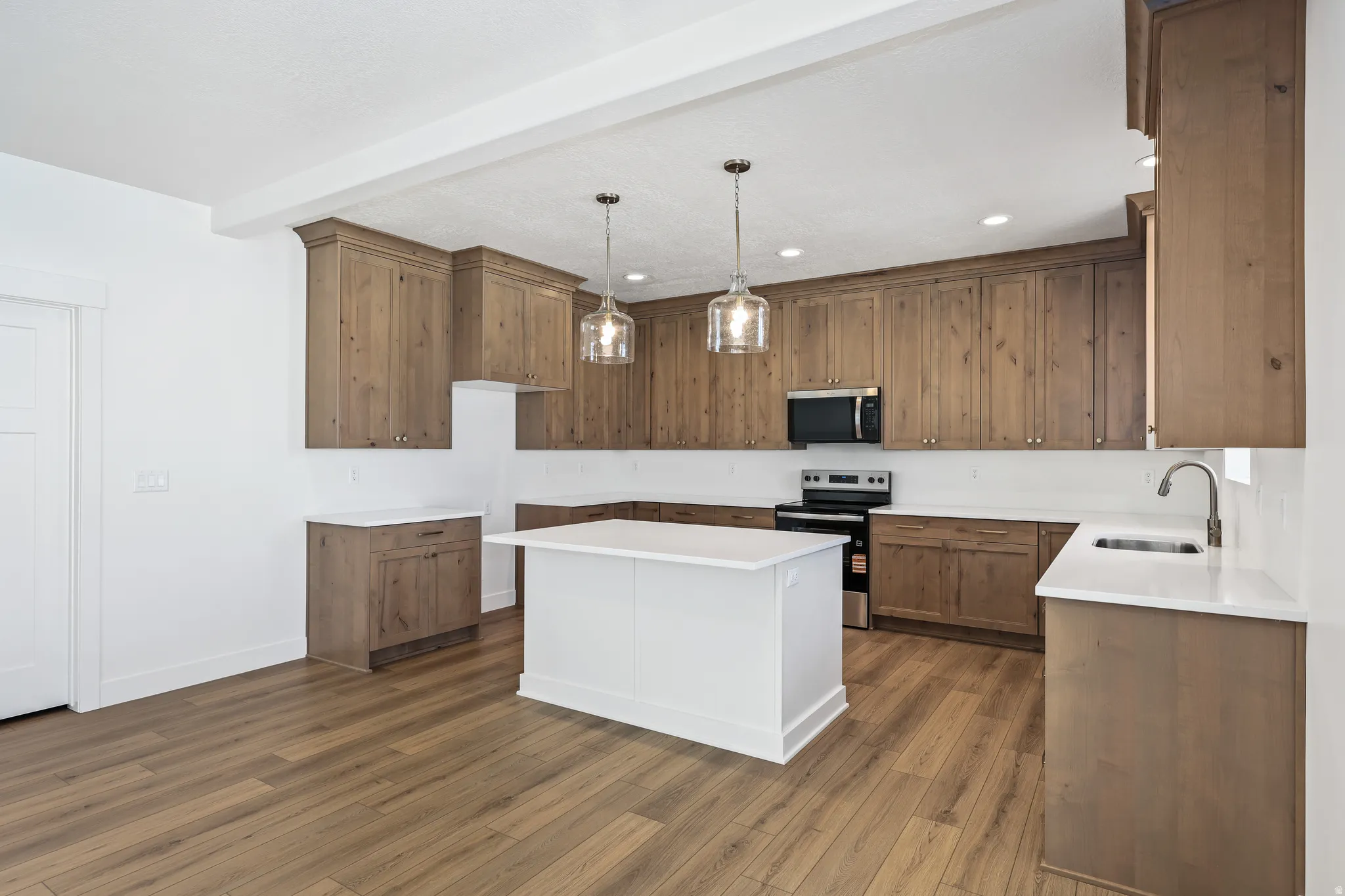 Kitchen with hanging light fixtures, stainless steel appliances, brown cabinetry, a center island, and dark wood finished floors
