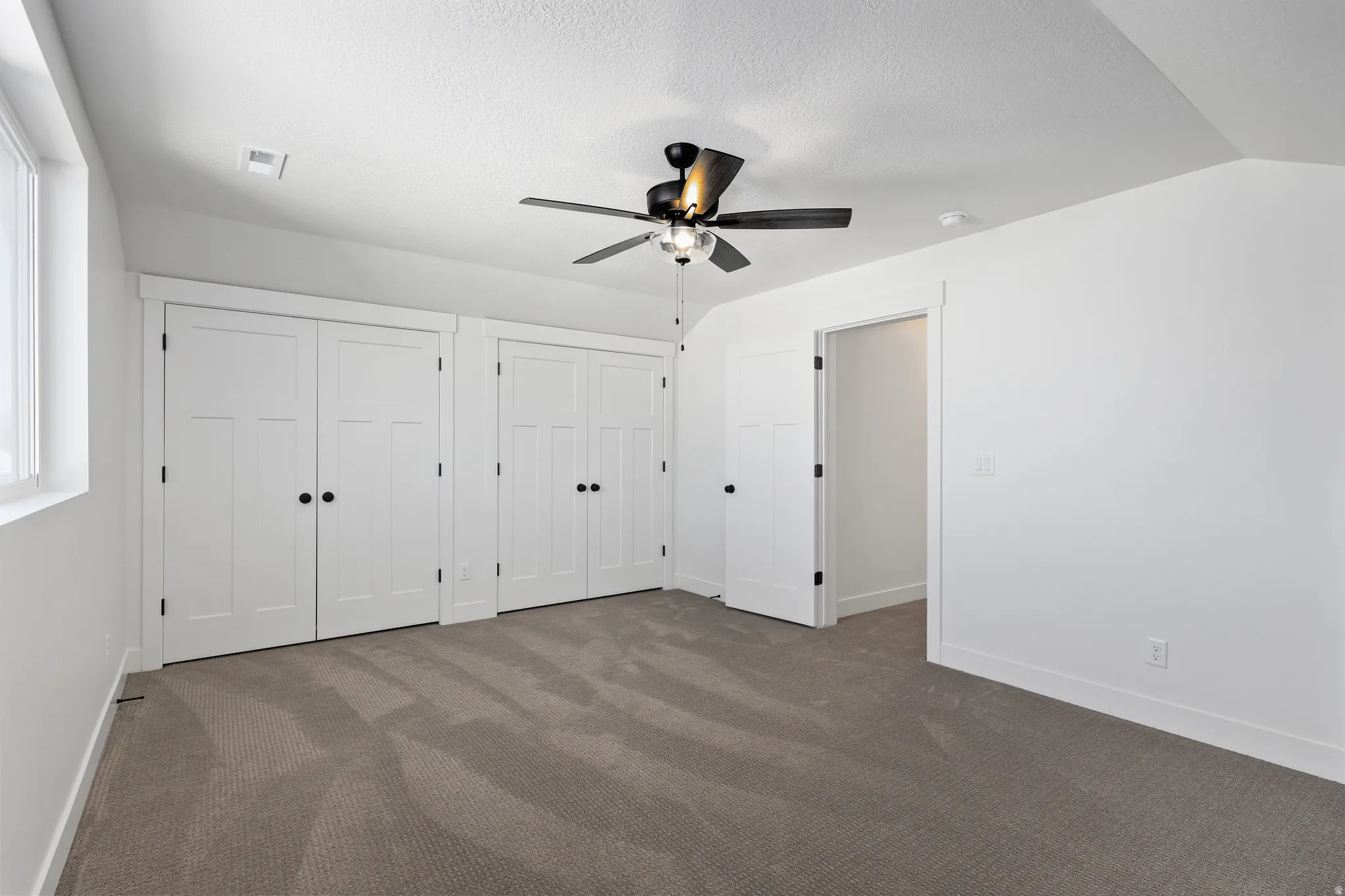 Unfurnished bedroom featuring two closets, carpet floors, a ceiling fan, and a textured ceiling