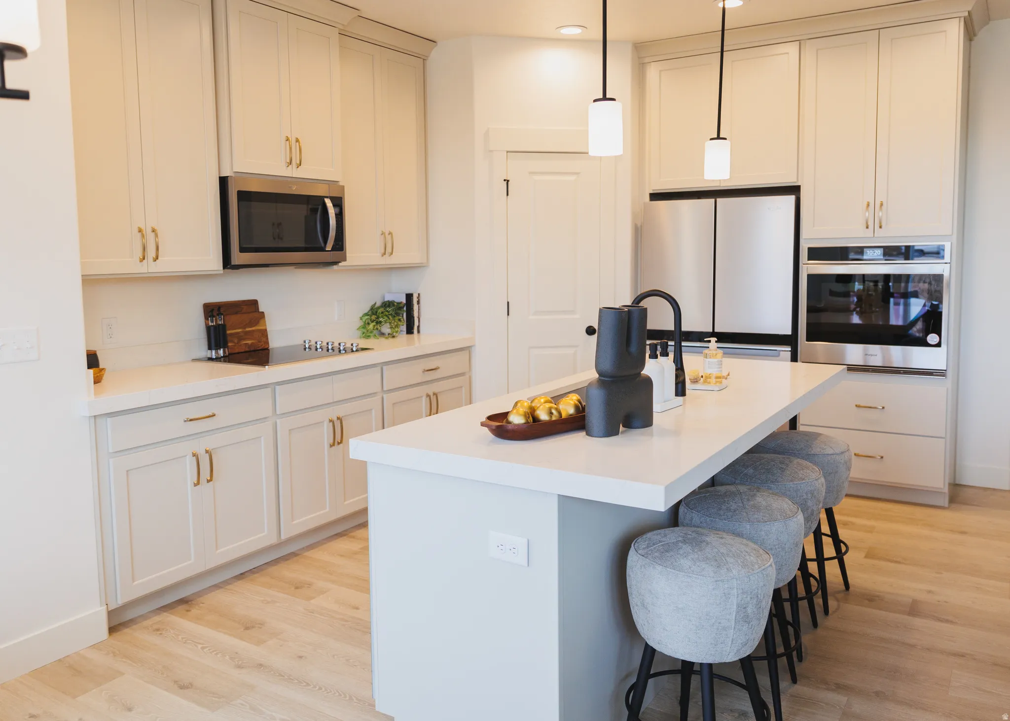 Kitchen with stainless steel appliances, a breakfast bar area, decorative light fixtures, a center island with sink, and light wood-style floors