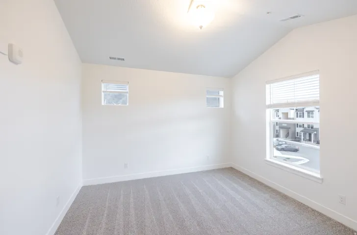 Empty room featuring light colored carpet and lofted ceiling