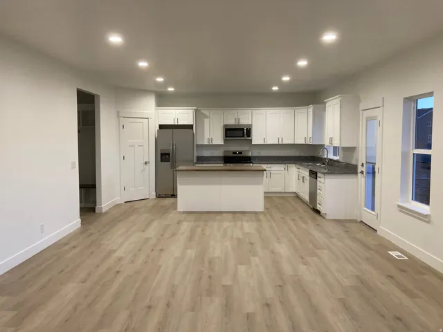 Kitchen featuring dark countertops, recessed lighting, white cabinetry, light LVP floors, and stainless steel appliances
