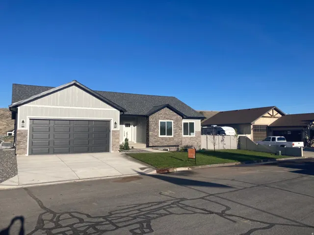 View of front facade featuring a garage, concrete driveway, roof with shingles, and stone siding