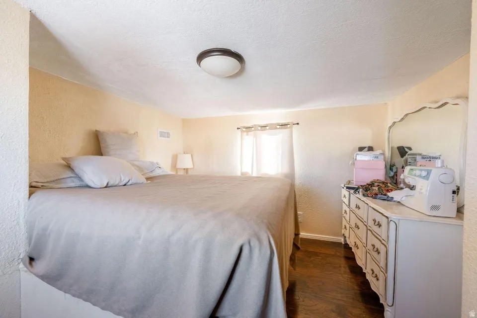 Bedroom with a textured wall, dark wood-style floors, and a textured ceiling