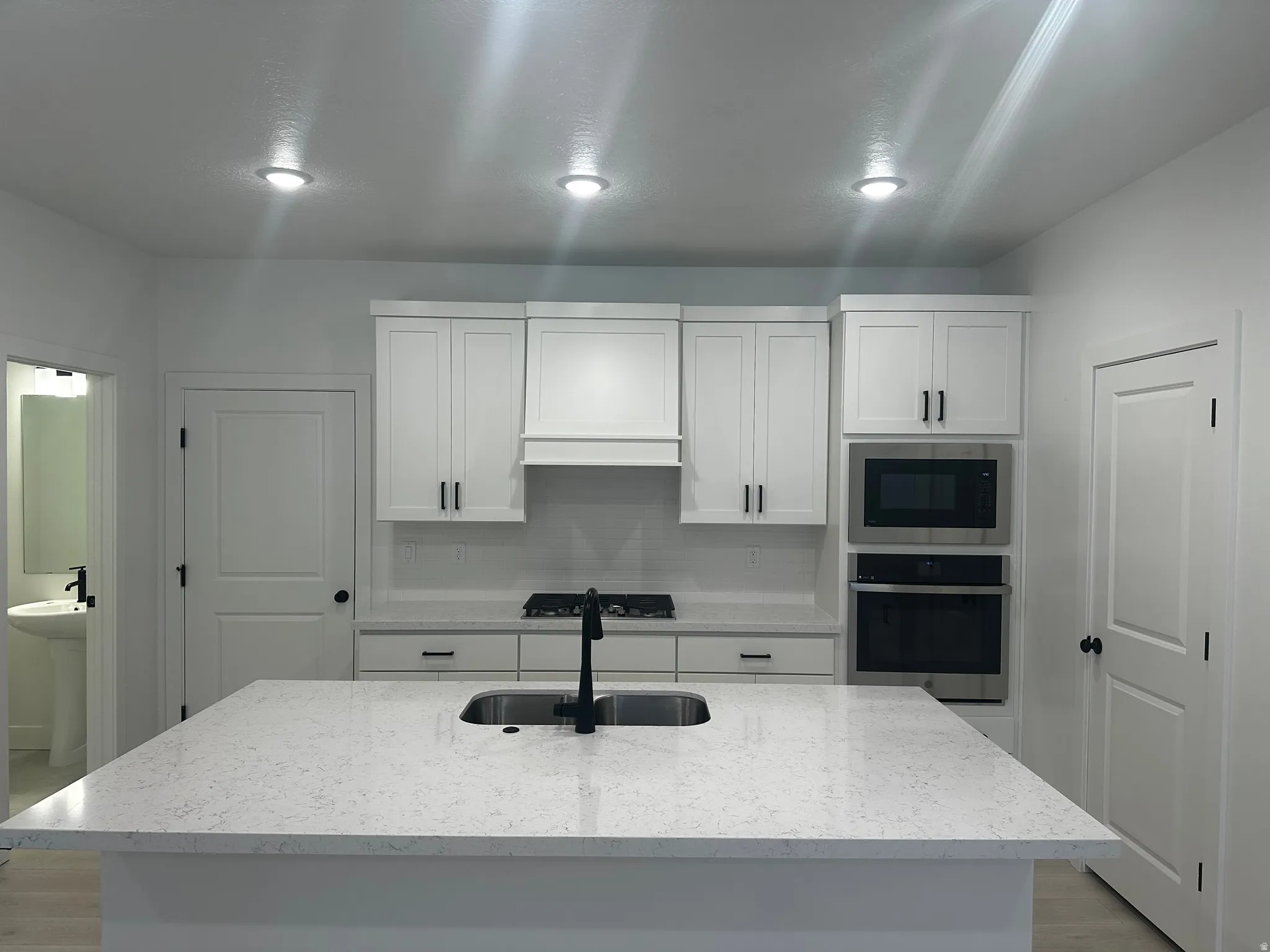 Kitchen featuring stainless steel appliances, light stone countertops, white cabinetry, a center island with sink, and tasteful backsplash