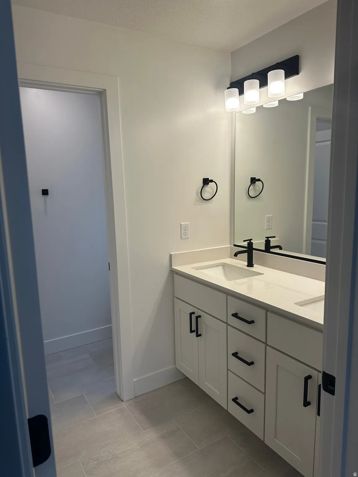 Bathroom with double vanity, a textured ceiling, and light tile patterned flooring