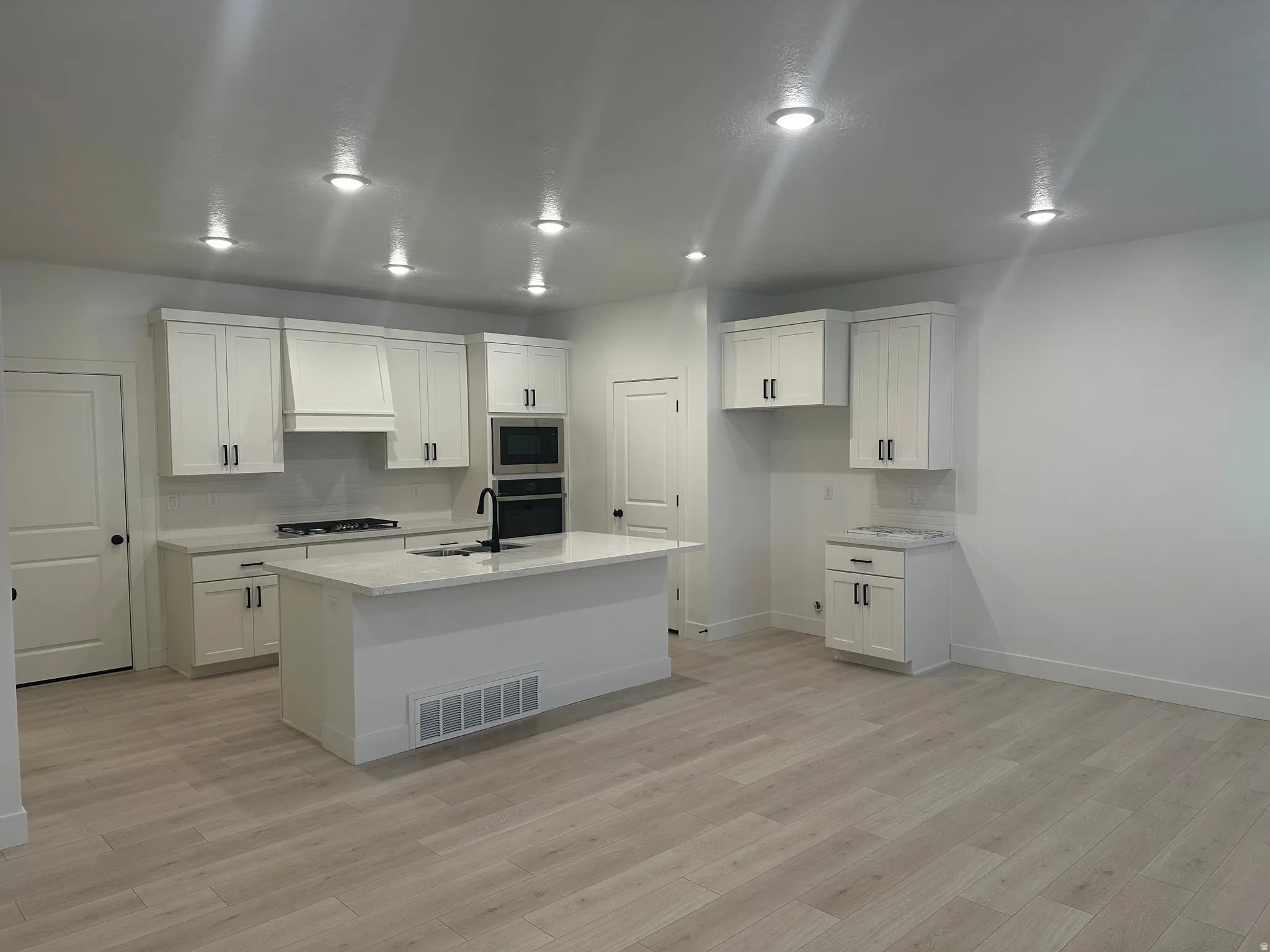 Kitchen featuring decorative backsplash, white cabinets, light stone counters, and recessed lighting