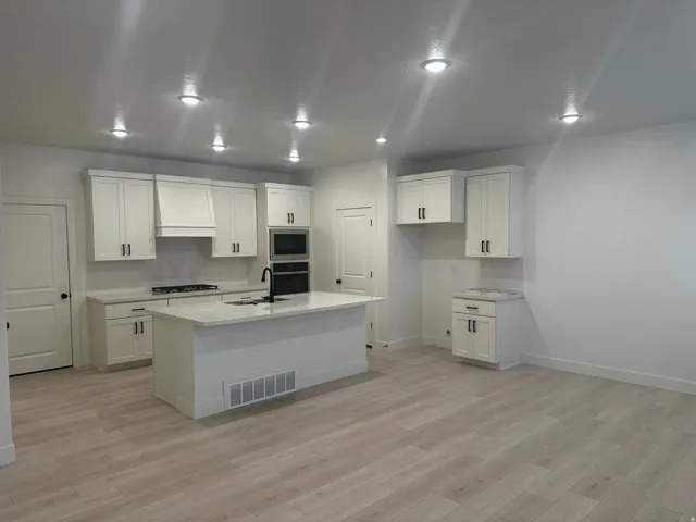 Kitchen featuring decorative backsplash, white cabinets, light stone counters, and recessed lighting