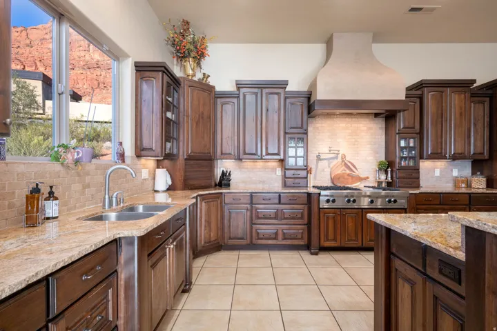 Kitchen with backsplash, light tile patterned flooring, light stone countertops, custom range hood, and dark brown cabinetry