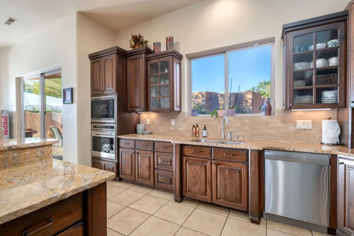 Kitchen with glass insert cabinets, light stone countertops, stainless steel appliances, backsplash, and light tile patterned flooring