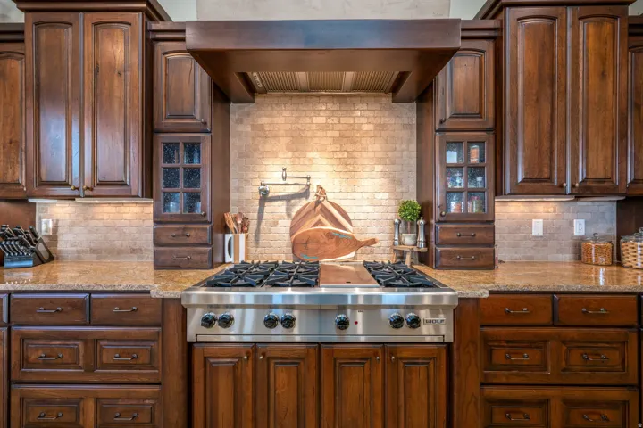 Kitchen featuring decorative backsplash, stainless steel gas cooktop, exhaust hood, light stone countertops, and dark brown cabinets
