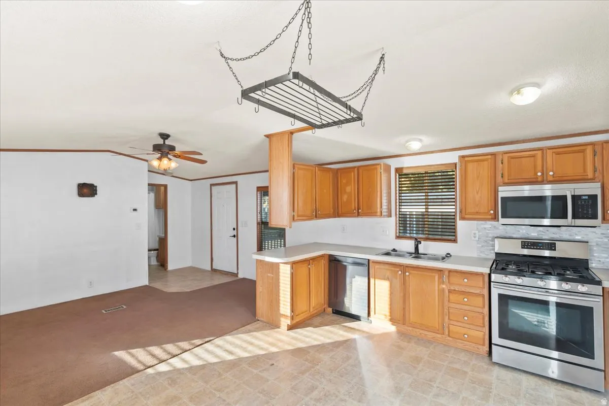 Kitchen with appliances with stainless steel finishes, crown molding, light countertops, backsplash, and light carpet