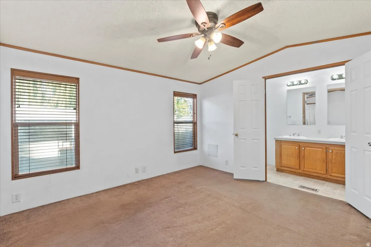 Unfurnished bedroom with light carpet, crown molding, a ceiling fan, lofted ceiling, and ensuite bath