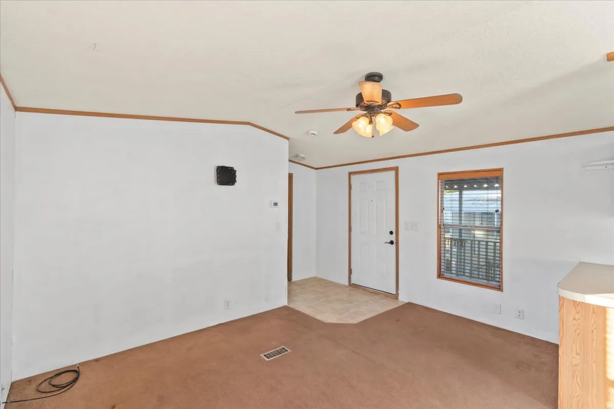 Empty room featuring crown molding, carpet floors, a ceiling fan, and lofted ceiling