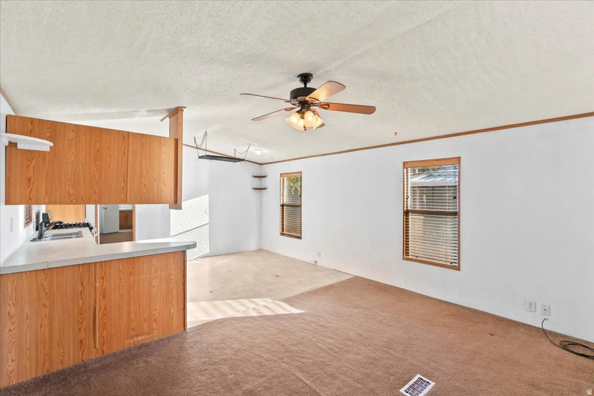 Kitchen with light colored carpet, light countertops, a textured ceiling, open floor plan, and ceiling fan