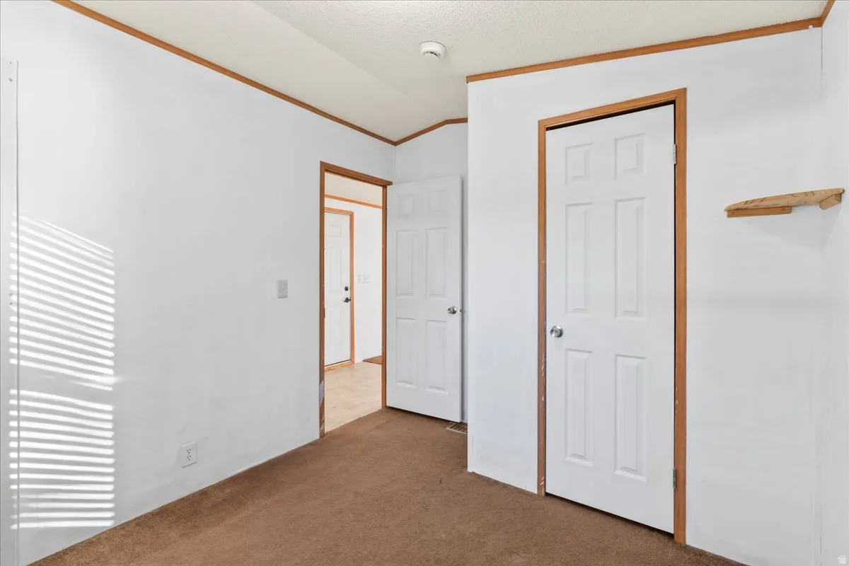 Unfurnished bedroom featuring crown molding, carpet flooring, vaulted ceiling, a closet, and a textured ceiling